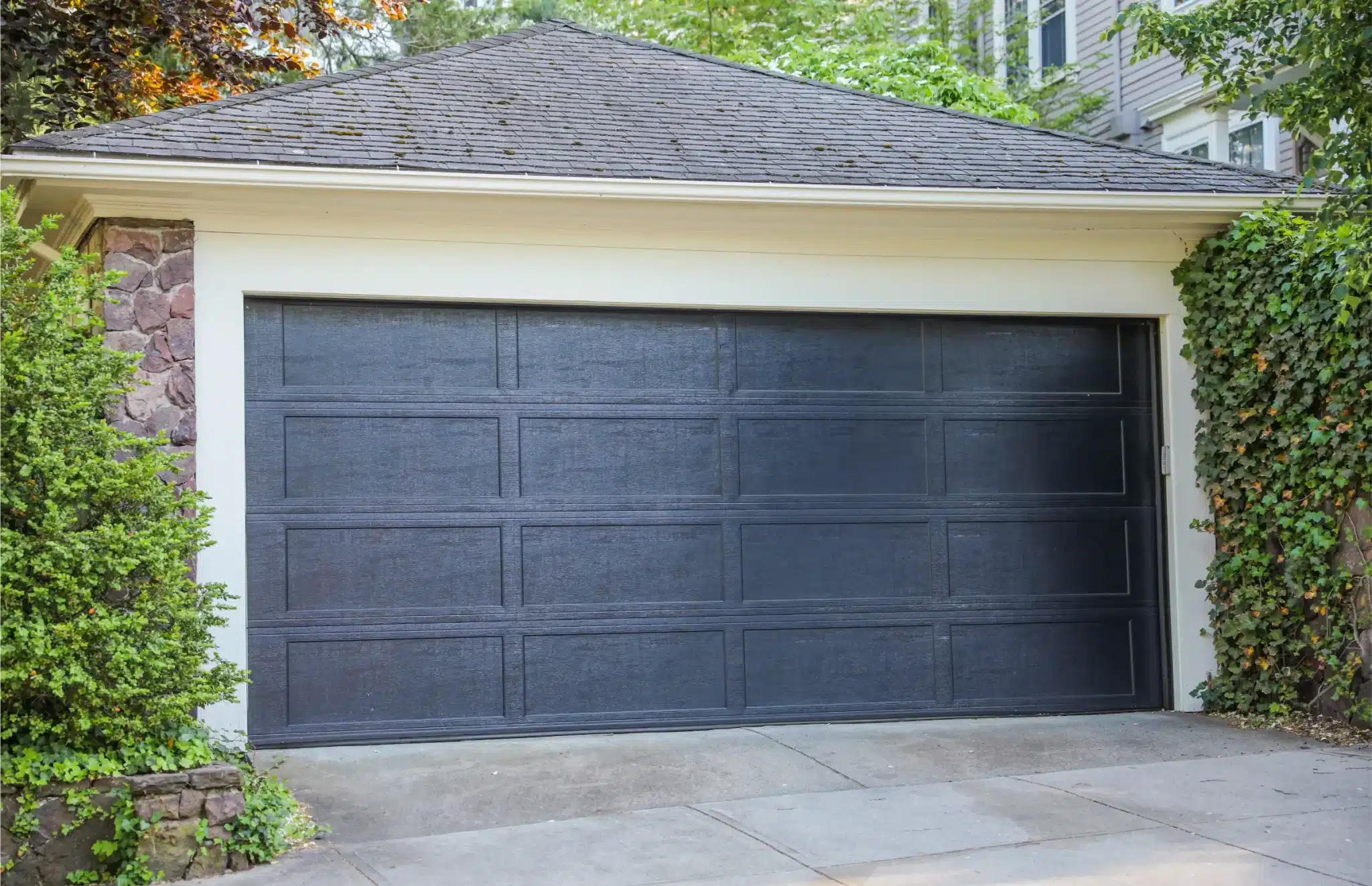 Black modern garage door surrounded by stone and greenery, ideal example for garage door repair services.