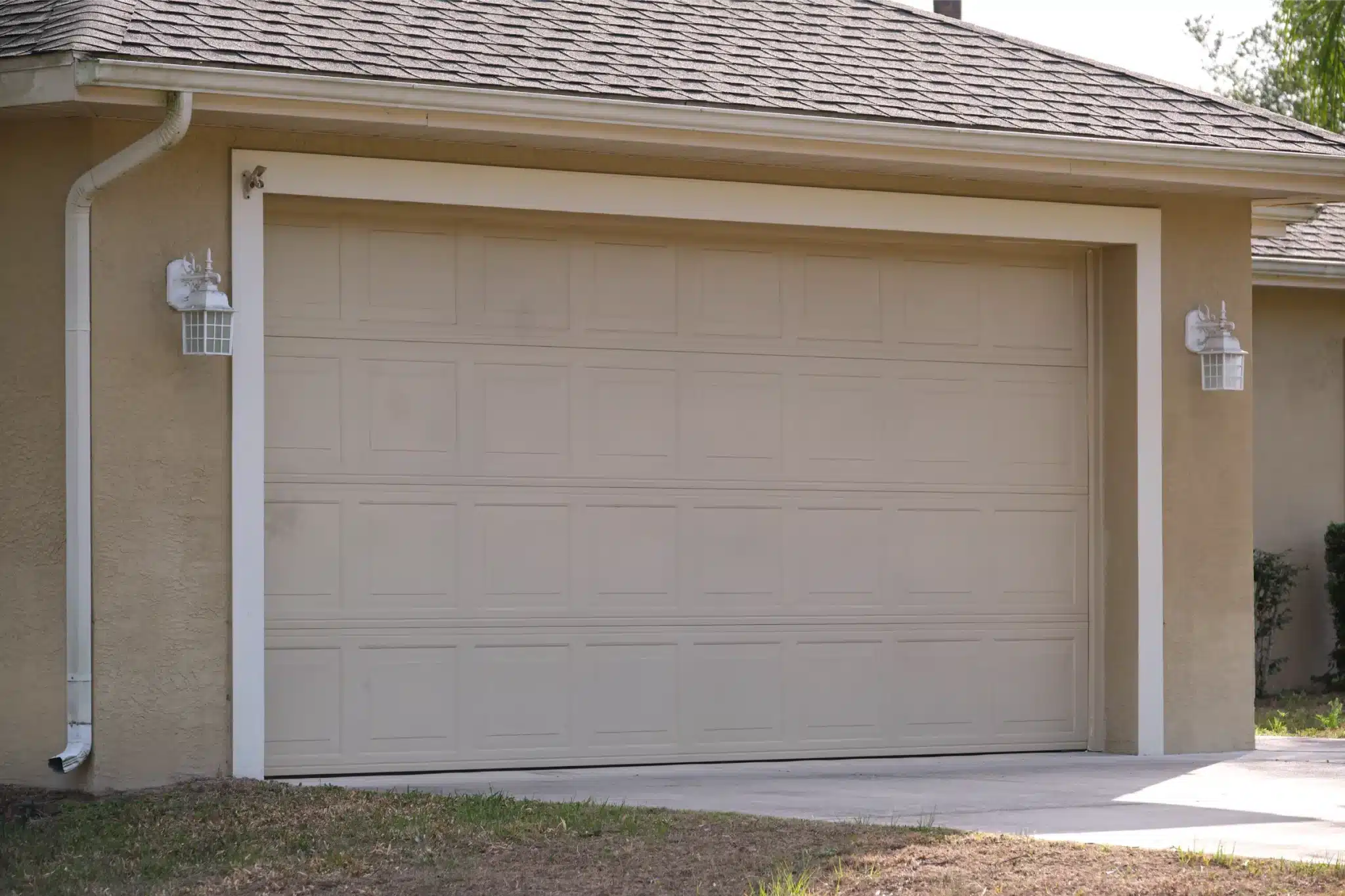 Beige residential garage door with raised panels on a suburban home serviced for garage door spring replacement.