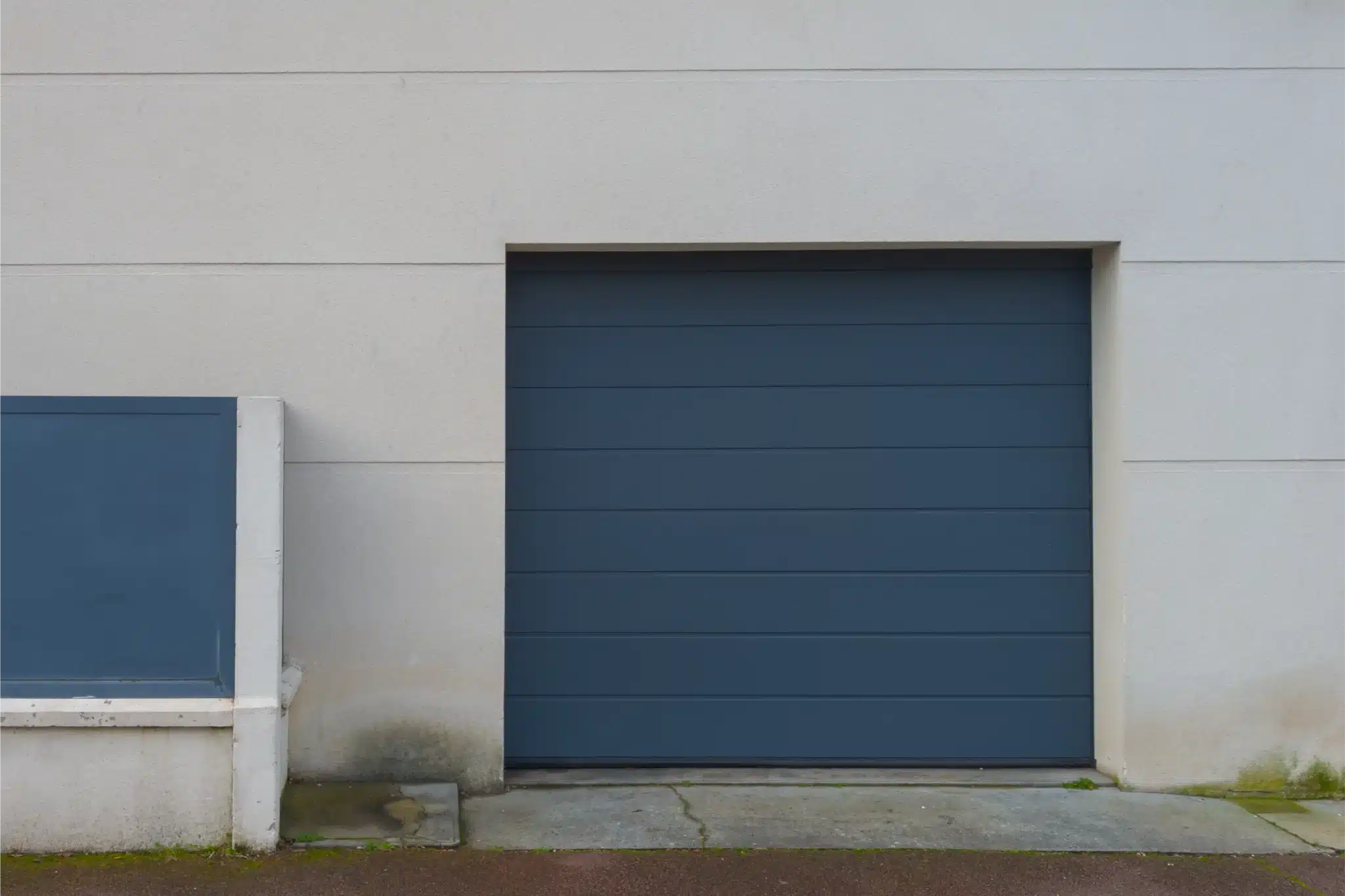Blue modern garage door with smooth panels set in light concrete wall, example for garage door panel replacement.
