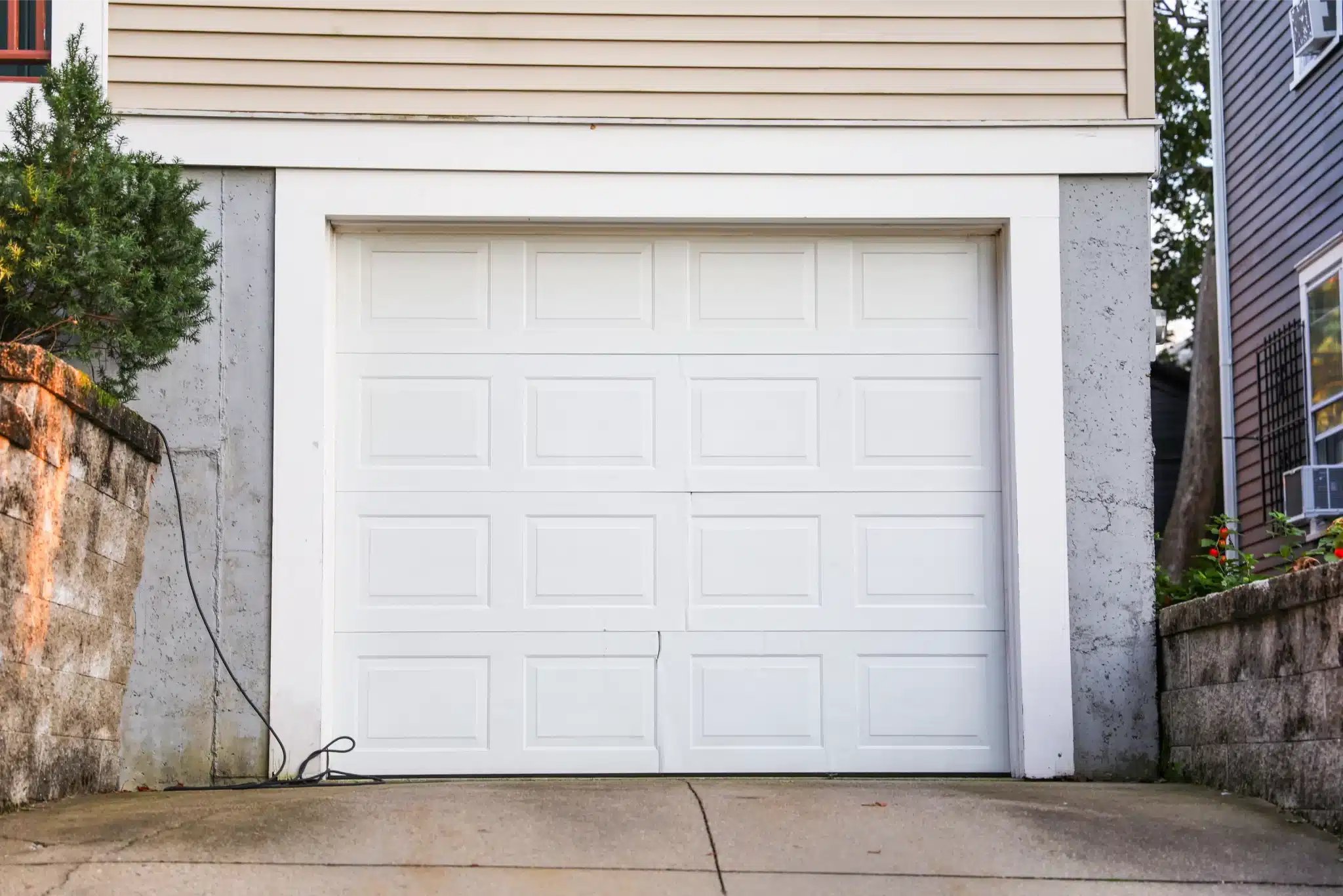 Single white garage door on sloped driveway with minor panel damage needing garage door repair services.
