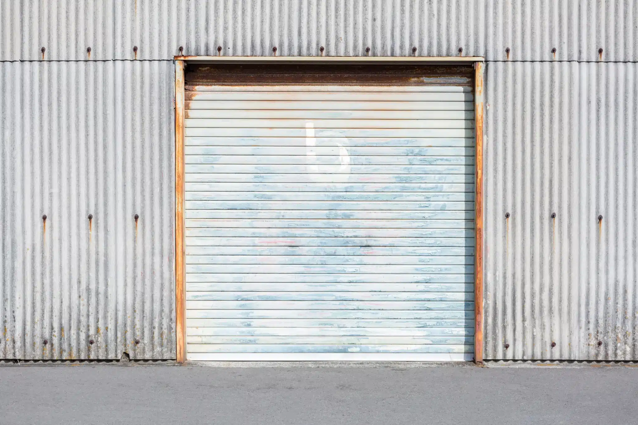 Old corrugated metal garage door with rusted edges and faded paint, suitable for garage door panel replacement.